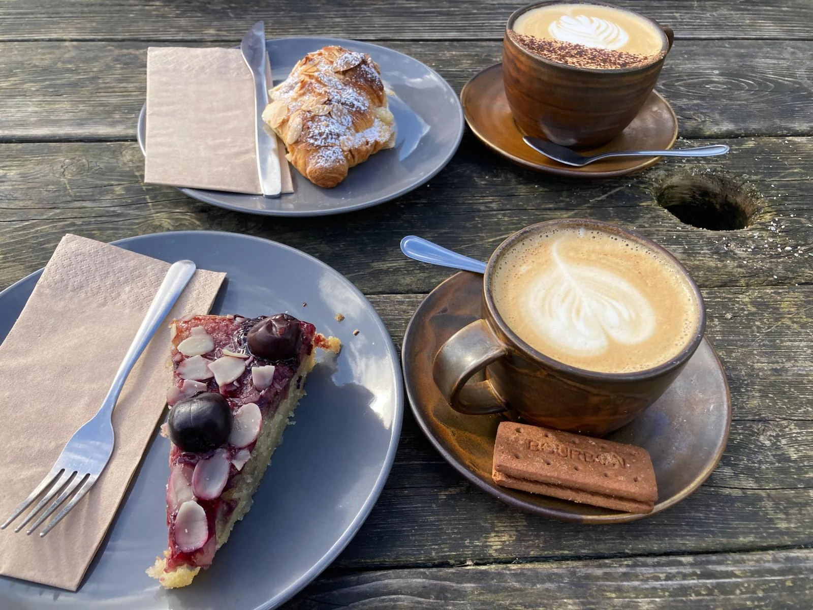 Coffee, cake and a croissant served on a weathered outdoor table at The Pier Cafe